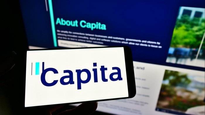 Capita fined £14mn over theft of personal data in cyber attack A person holds a smartphone displaying the Capita logo in front of a computer screen showing Capita's website.