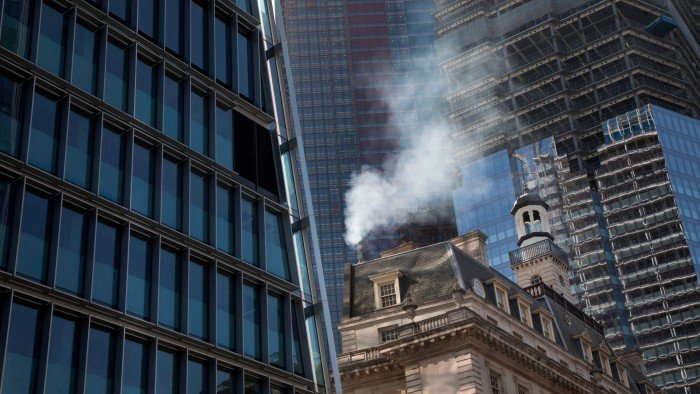 Property market faces green transition challenge Pollution from the chimney of an old building pours out into the sky among modern glass buildings in the City of London.