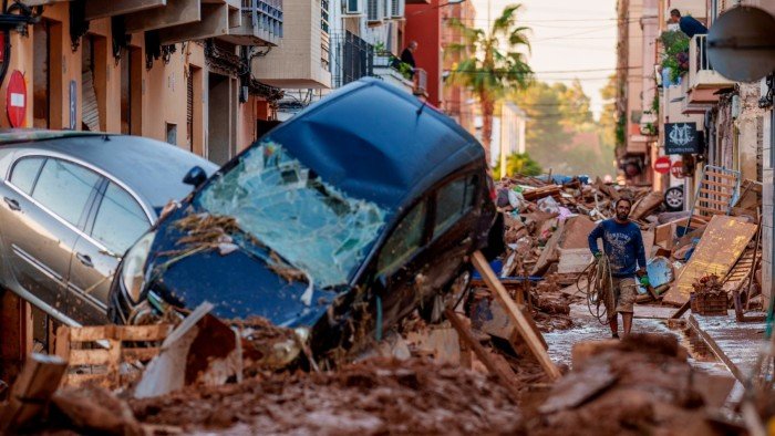Why insurers are taking up climate consulting A man walks through a street filled with mud, debris, and damaged cars after severe flooding in Valencia, Spain.