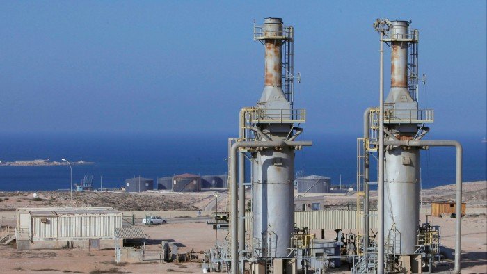 Oil majors return to Libya as Tripoli launches first exploration auction in 18 years Two large metal oil refinery towers with pipes and platforms stand at Marsa al Hariga oil port, with storage tanks and the sea in the background.