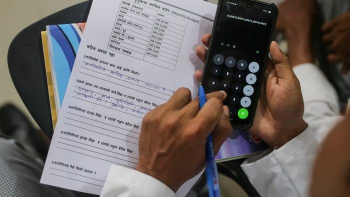 why financial education has never been more crucial View of a person’s hands while they do calculations on their phone calculator and fill in notes on coursework