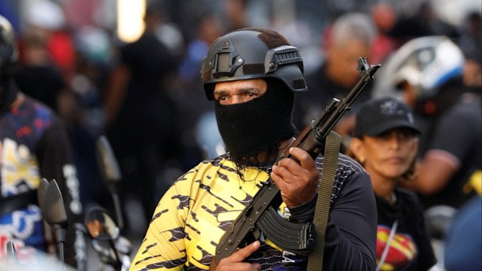 Venezuela launches wave of repression A member of the Colectivos militia wearing a helmet and face covering holds a rifle during a march, with others blurred in the background.